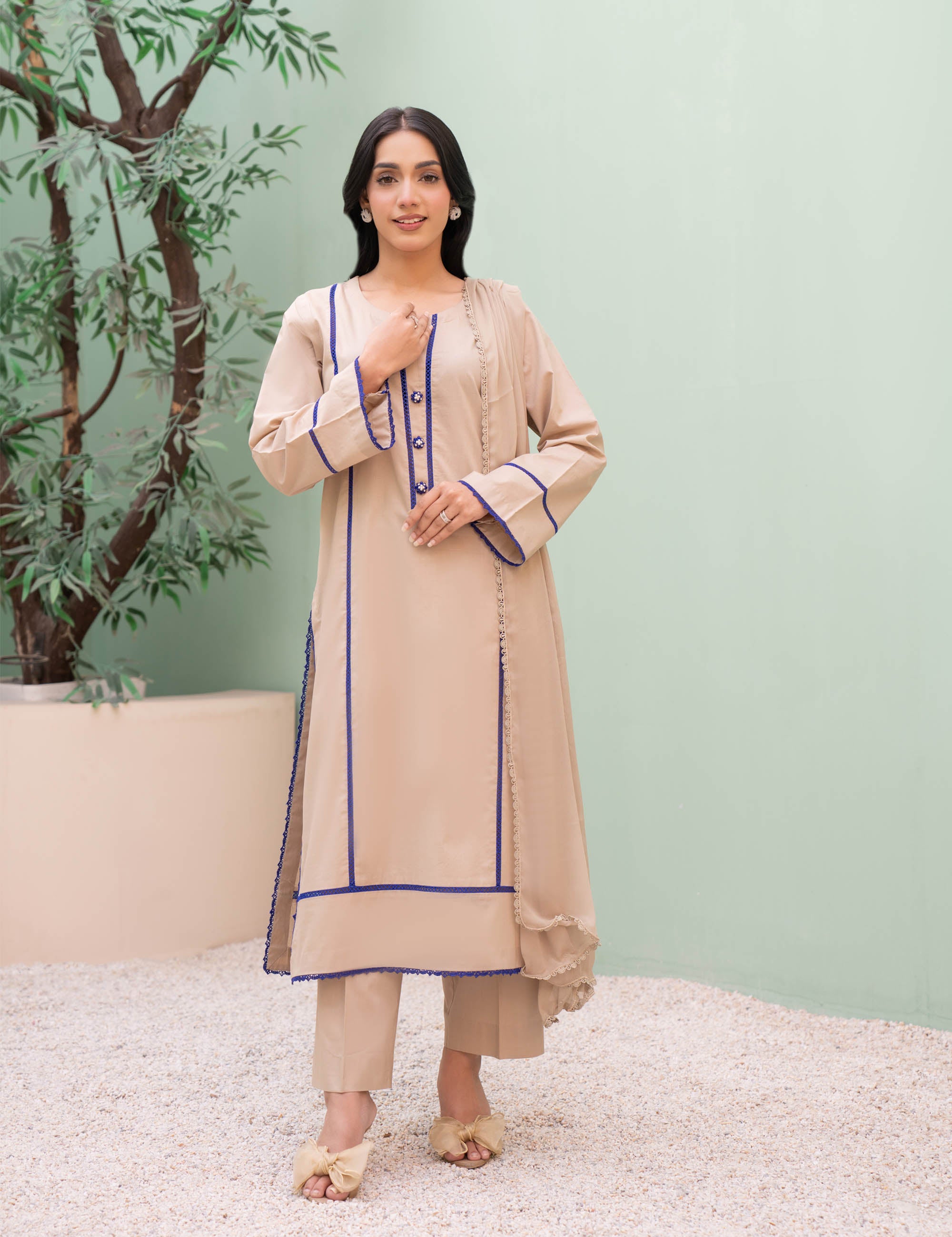 Woman wearing a beige traditional outfit with blue accents against a light green background